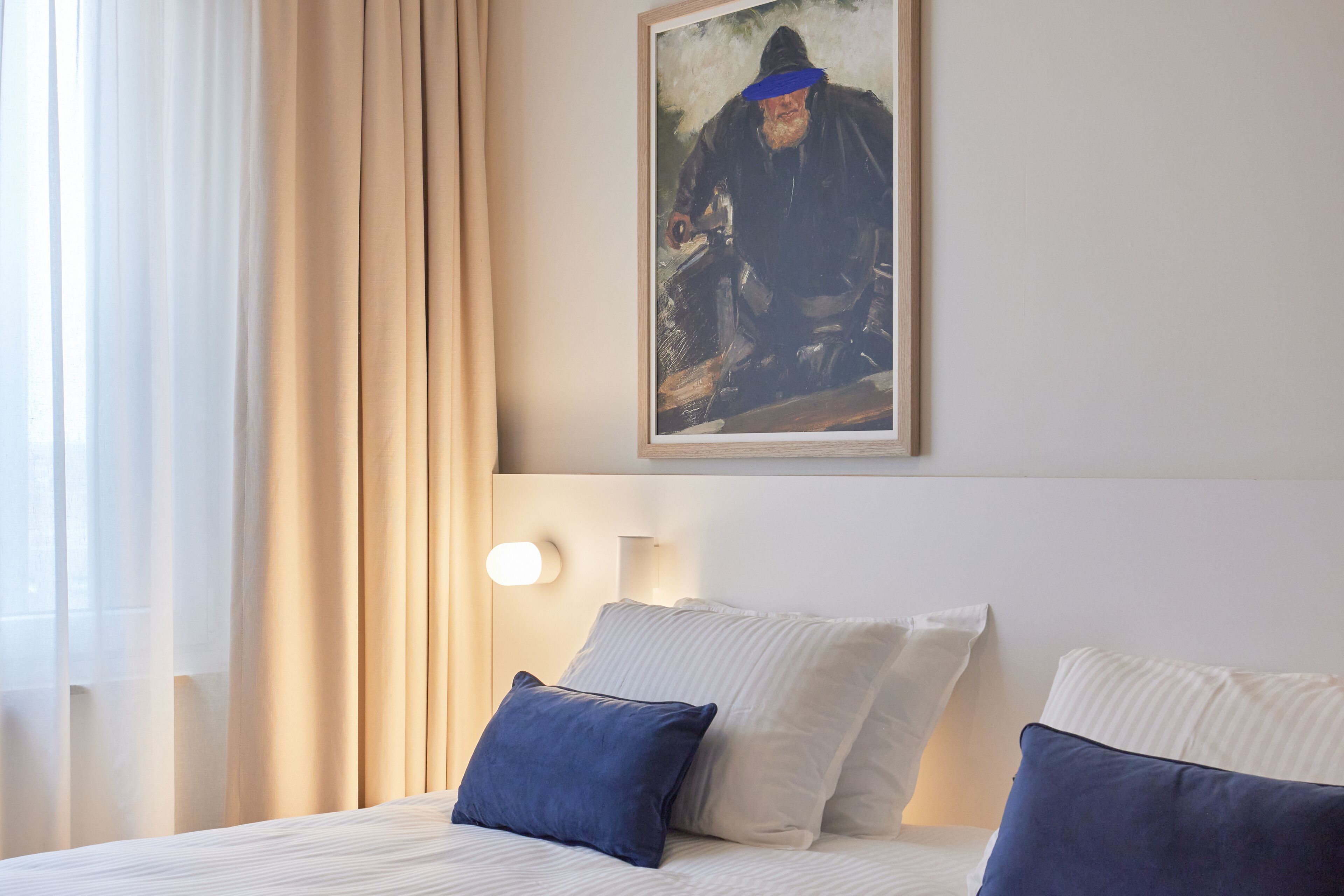 A hotel room with a bed, two pillows, a painting on the wall, and a window with curtains.