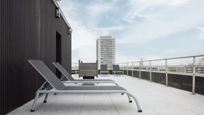 Terraza en la azotea con dos sillones, un muro de piedra y vista a un edificio alto al fondo.