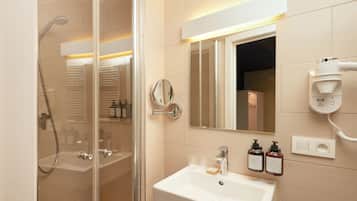 A modern bathroom with a glass-enclosed shower, a white sink, and a mirror above it. There are two bottles of shampoo and a soap dispenser on the sink.