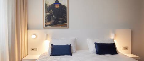 Habitación de hotel con una cama grande, dos mesitas de noche, un cuadro en la pared y una cortina a la izquierda.