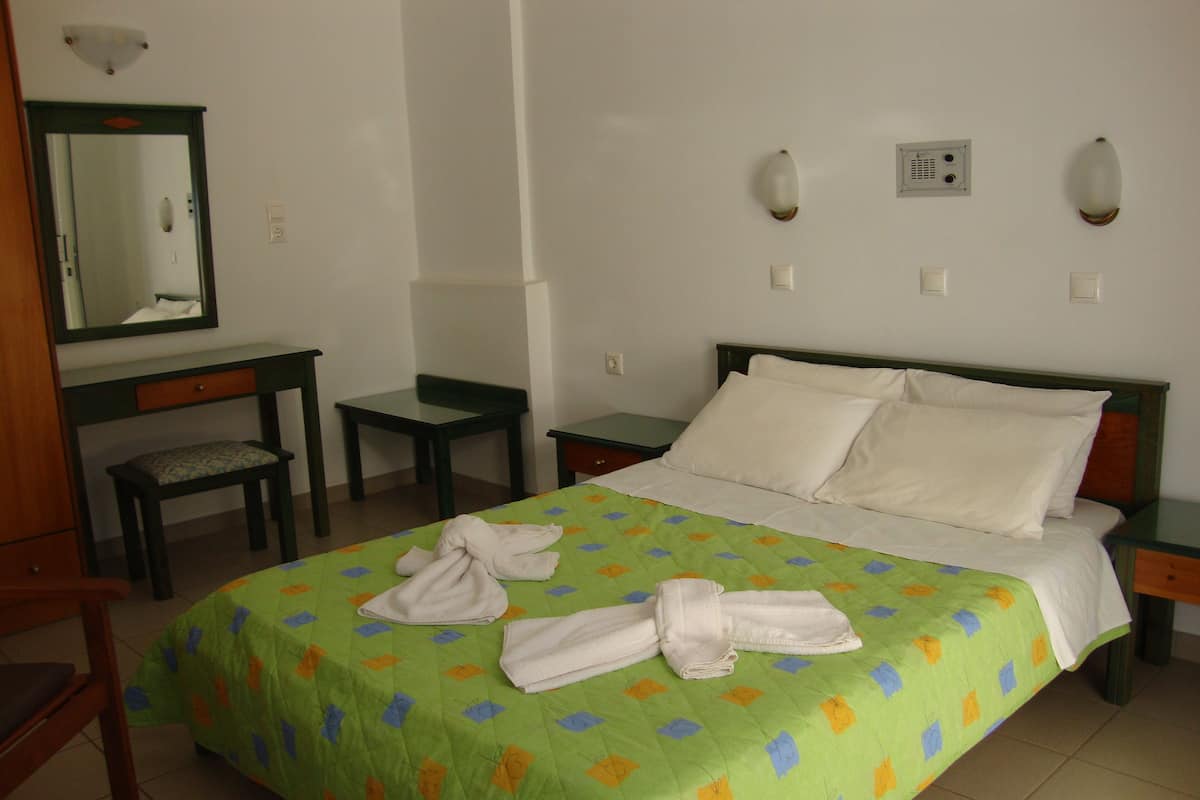 A hotel room with a bed, a desk, a chair, and a mirror.
