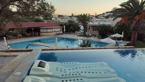 A pool area with a hot tub and lounge chairs, surrounded by palm trees and a view of the city. - Hotel Kyriaki (Chania)