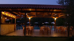 An outdoor dining area with tables and chairs, a pool, and a covered section with a bar. - Hotel Kyriaki (Chania)