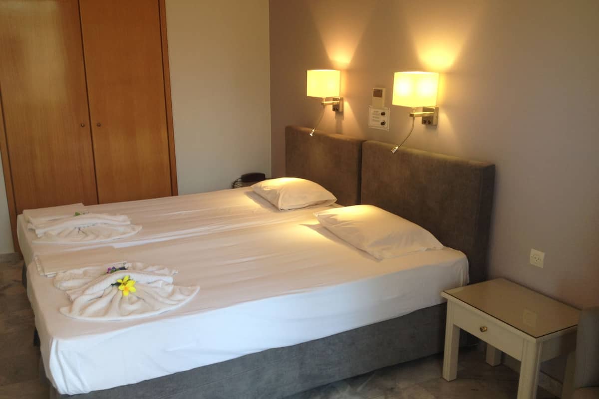 A hotel room with a double bed, two bedside lamps, a small bedside table, and a wooden wardrobe.
