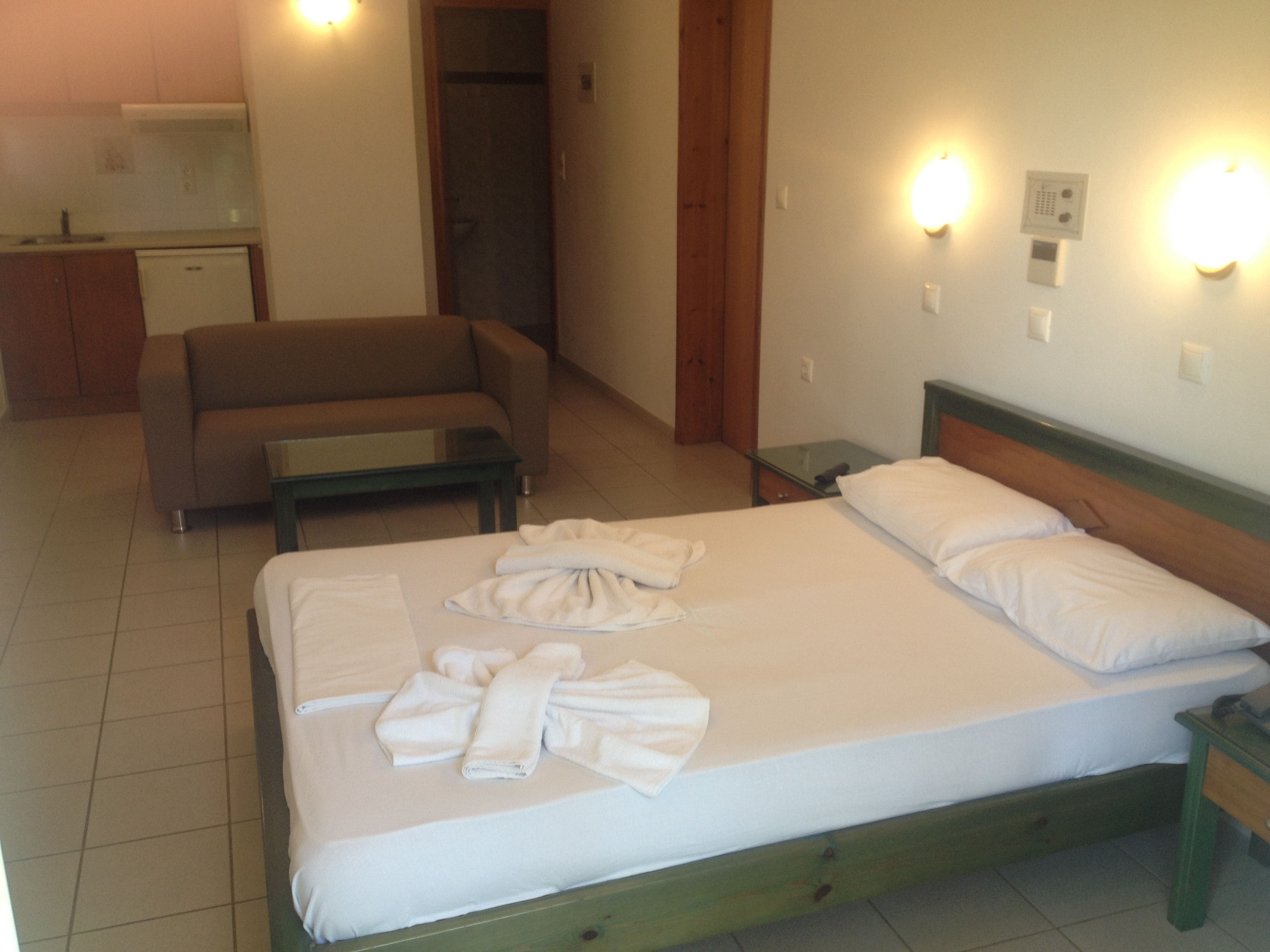A hotel room with a bed, a sofa, a small table, and a kitchenette in the background.