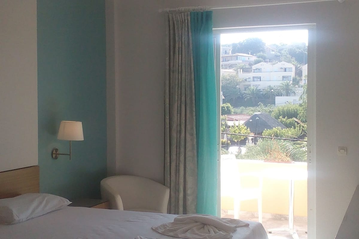 A hotel room with a bed, a chair, a lamp, and a view of the outside.