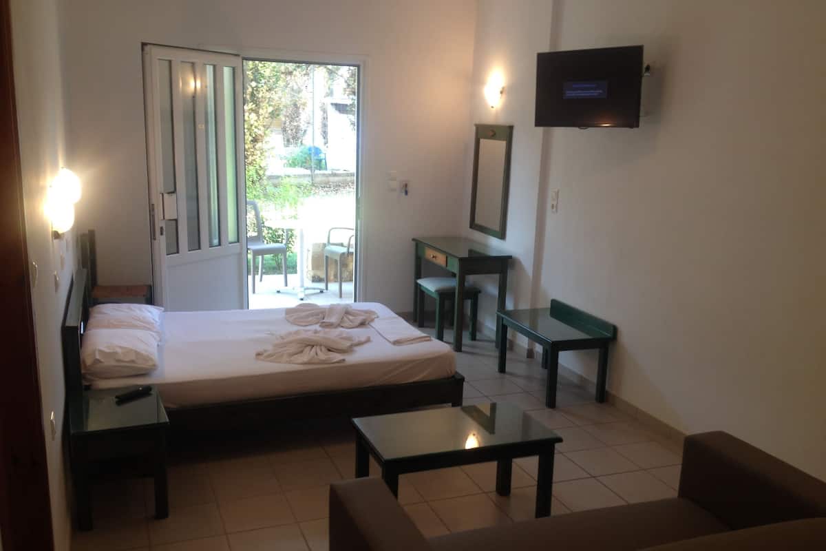 A hotel room with a bed, a desk, a chair, a sofa, and a TV on the wall.