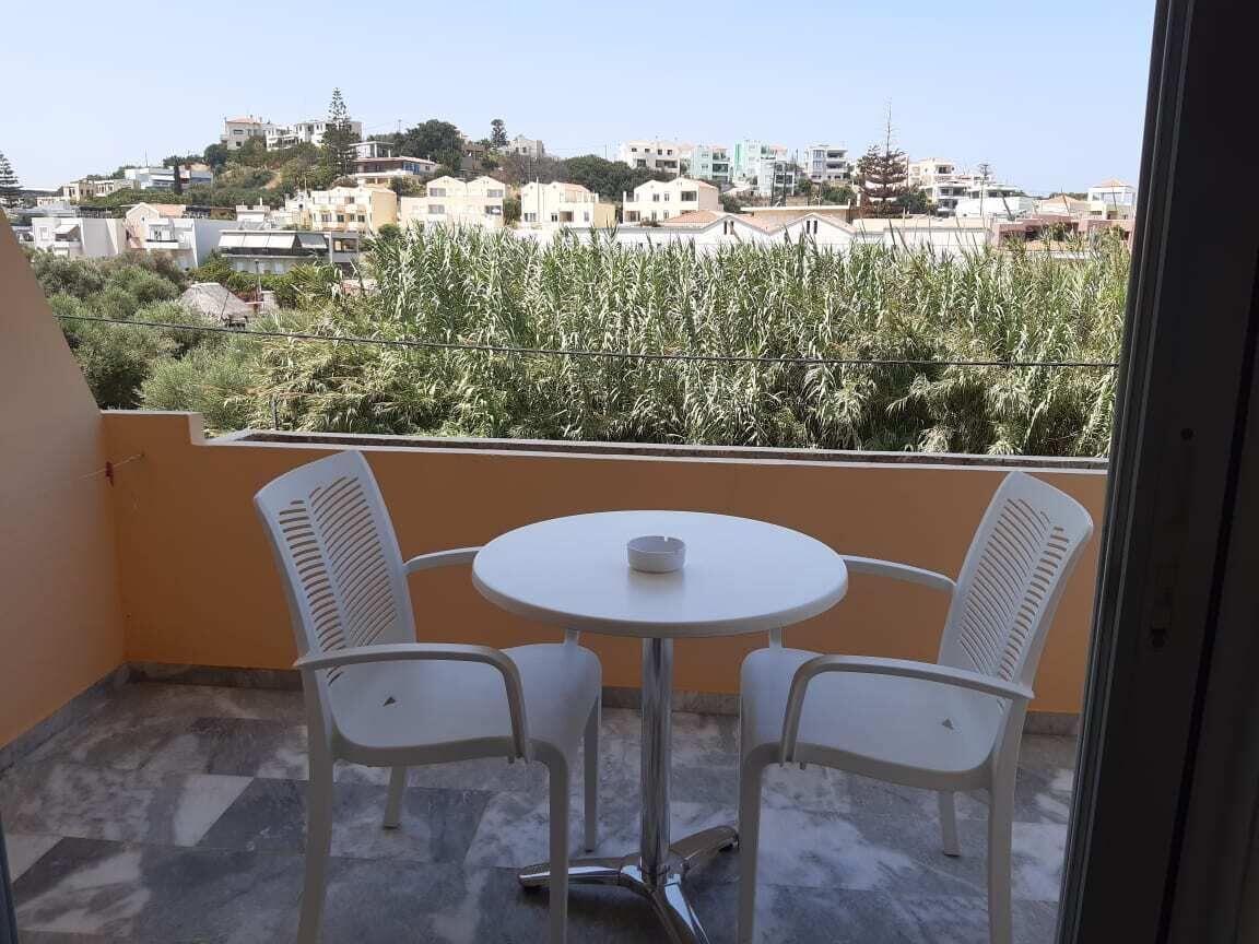 A balcony with a round table and two chairs, overlooking a residential area with houses and greenery.