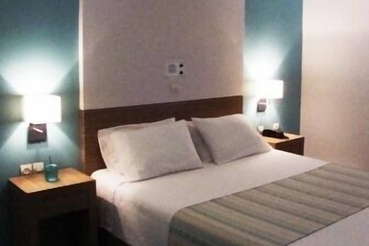 A hotel room with a bed, two bedside tables, and a nightstand.