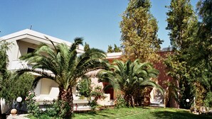 A building with a white facade, palm trees, and a red building in the background. - Hotel Kyriaki (Chania)