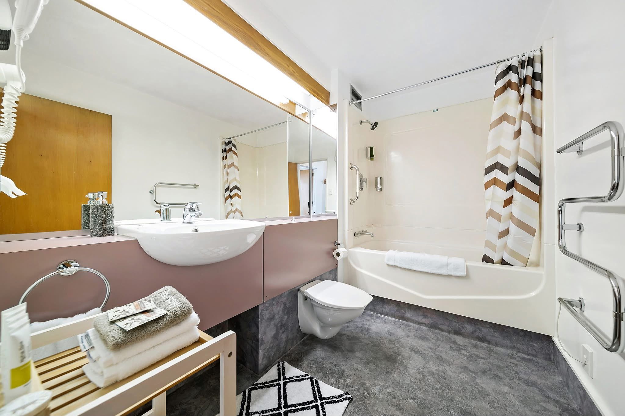 A modern bathroom with a vanity, sink, mirror, toilet, and bathtub.