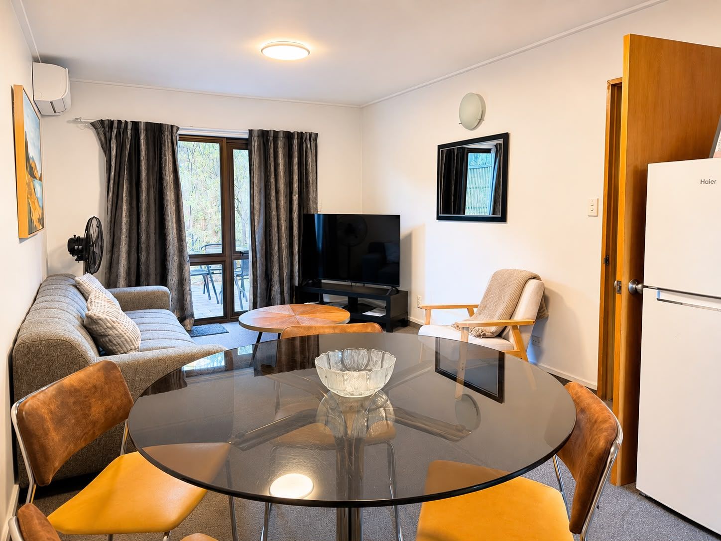 Un salón moderno con una mesa de vidrio, sofá, sillas, un televisor y una puerta con la etiqueta 'Haier'.
