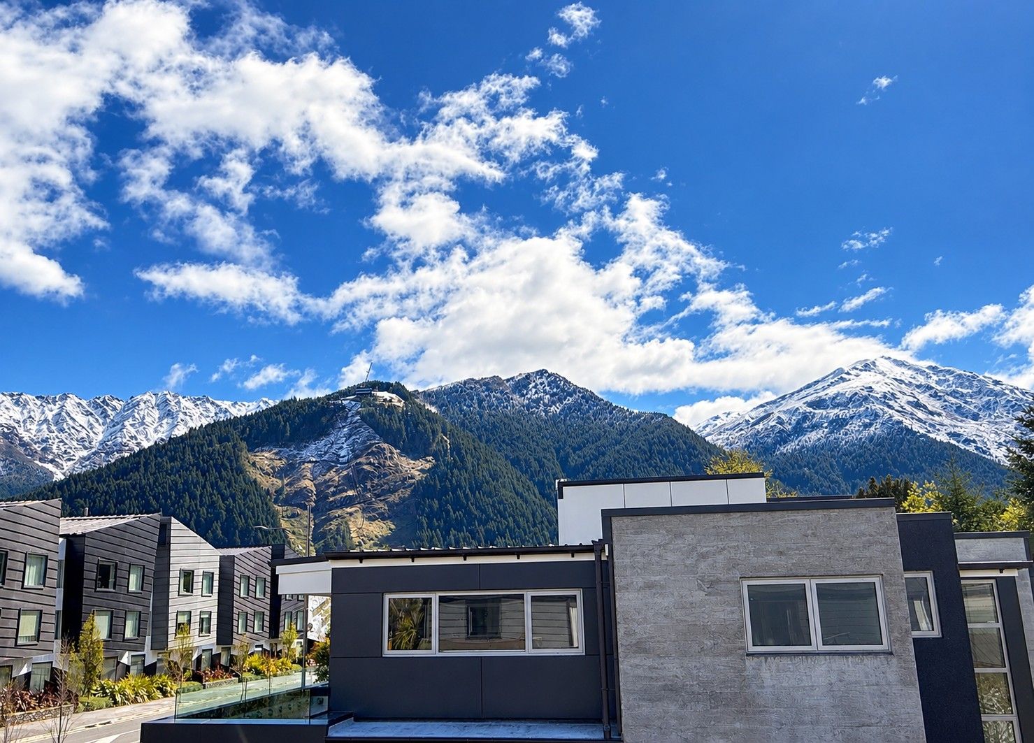 A modern building with a flat roof and large windows, set against a backdrop of snow-capped mountains and a clear blue sky.