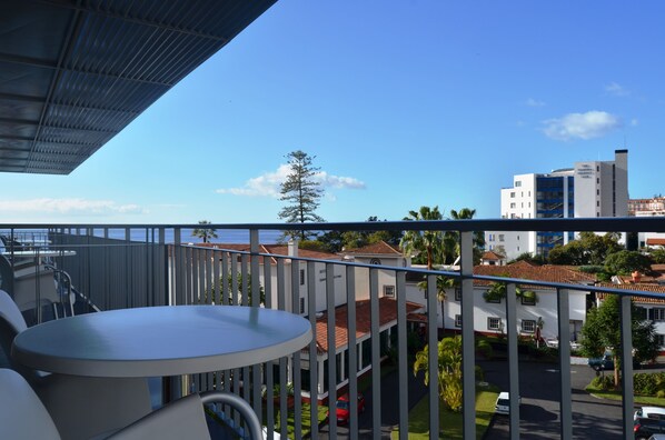 A balcony with a table and chairs, overlooking a street with buildings and a clear sky. - Madeira Bright Star Hotel (Funchal)