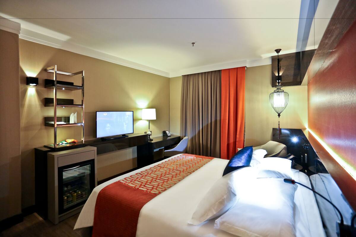 A hotel room with a bed, a desk with a computer, a television, and a minibar.