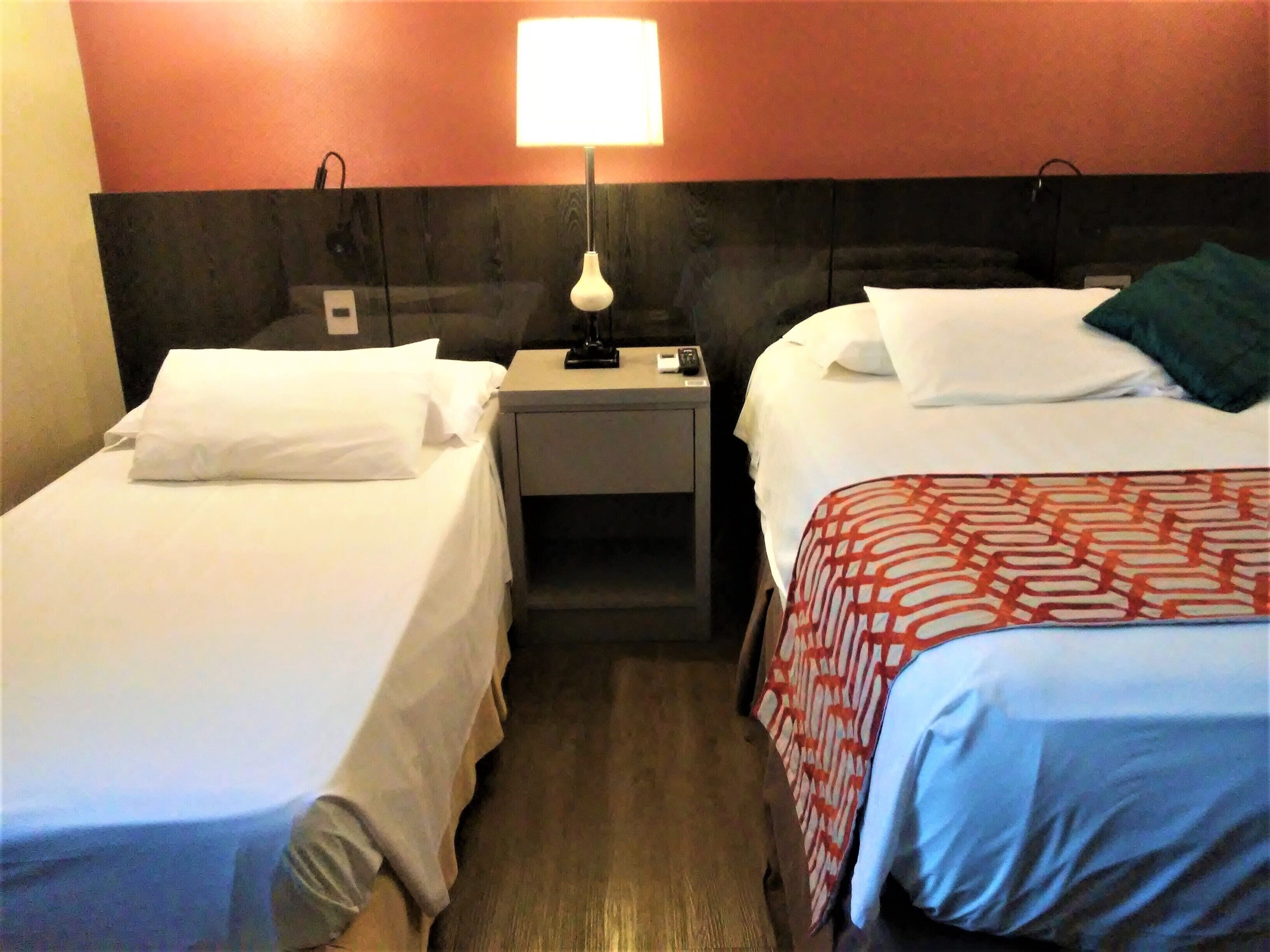 A hotel room with two single beds, a nightstand with a lamp, and a wooden floor.