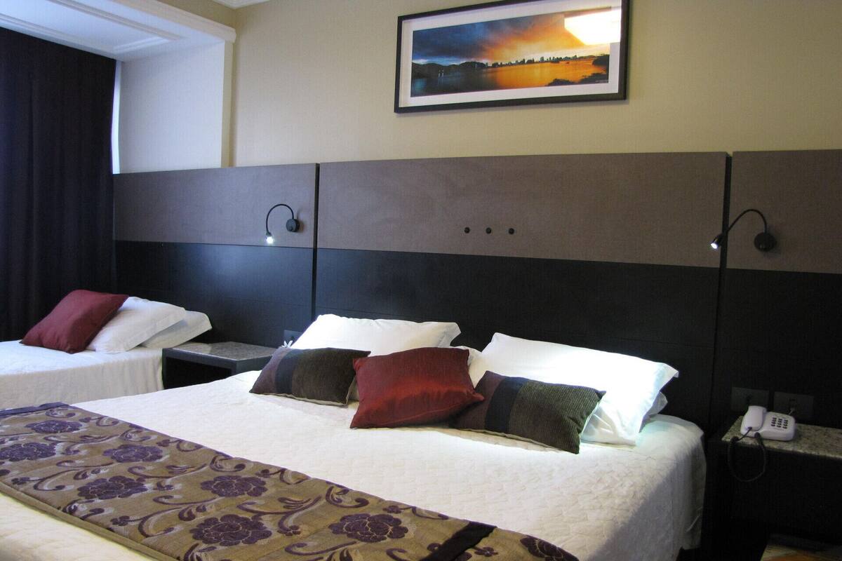 A hotel room with two beds, a large window, a painting on the wall, and a telephone on the nightstand.