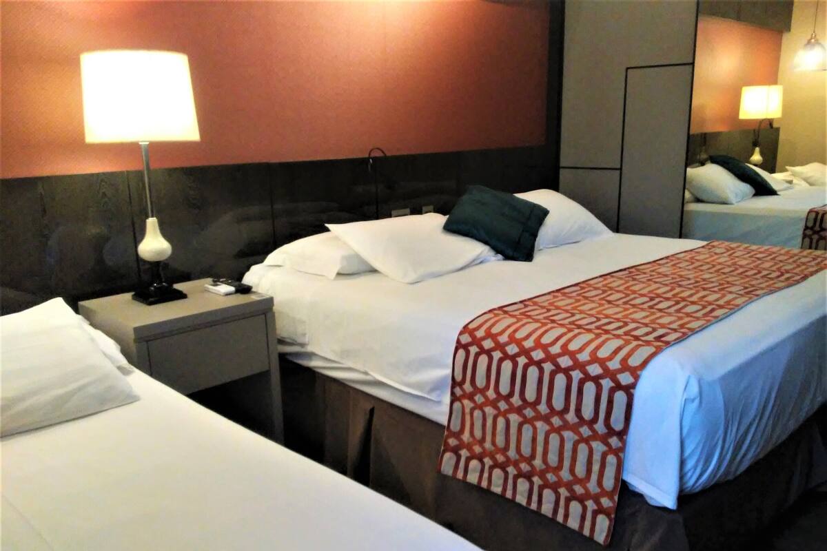 A hotel room with two beds, a nightstand with a lamp, and a mirror.