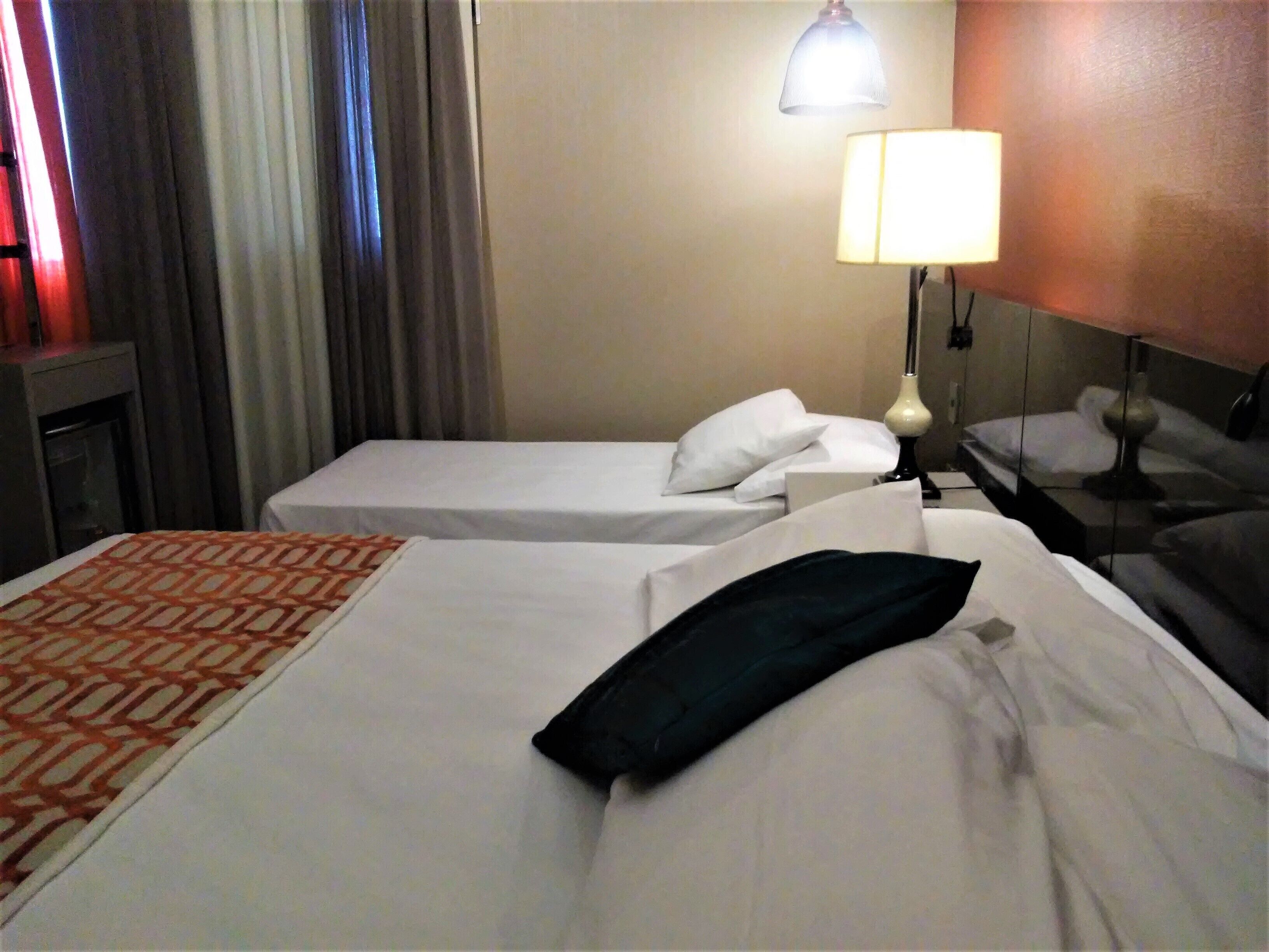 A hotel room with two single beds, a lamp, and a nightstand.