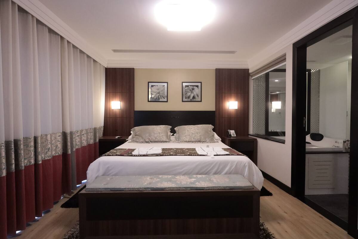 A hotel room with a large bed, two bedside tables, a mirror, and a wardrobe.