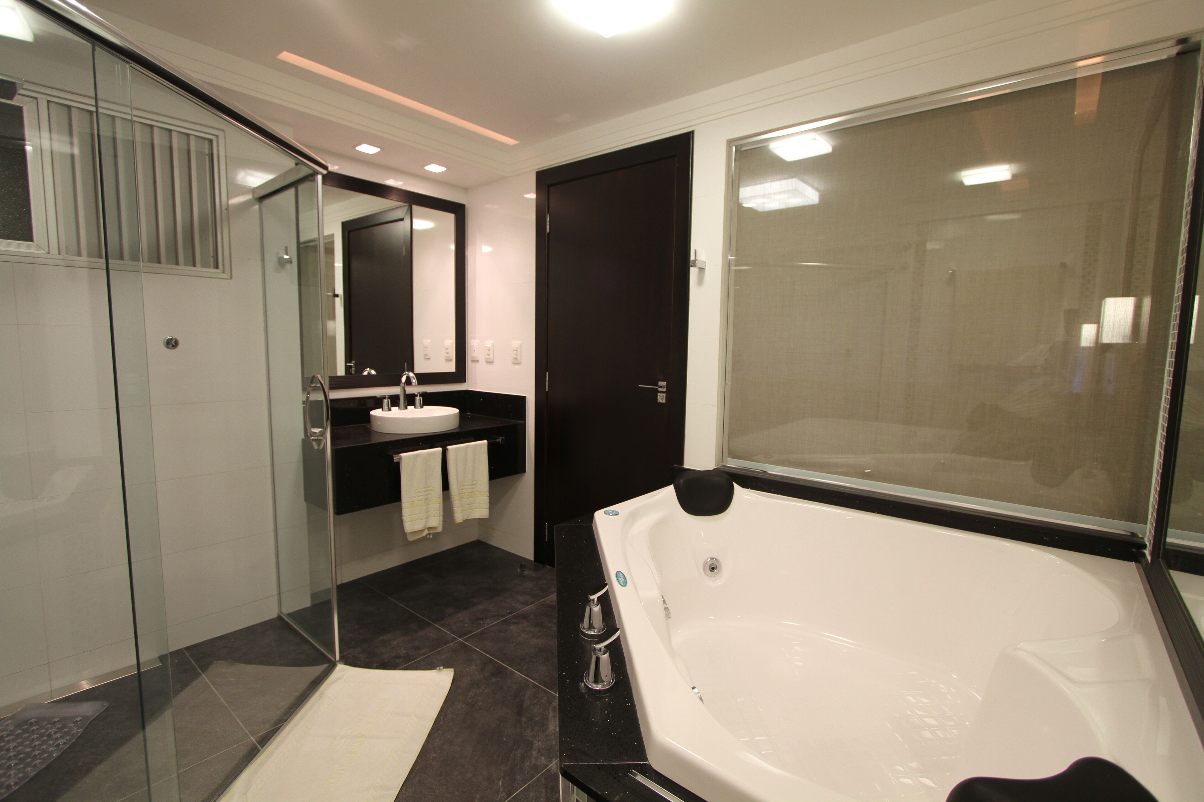 A modern bathroom with a glass-enclosed shower, a large bathtub, and a separate sink area.