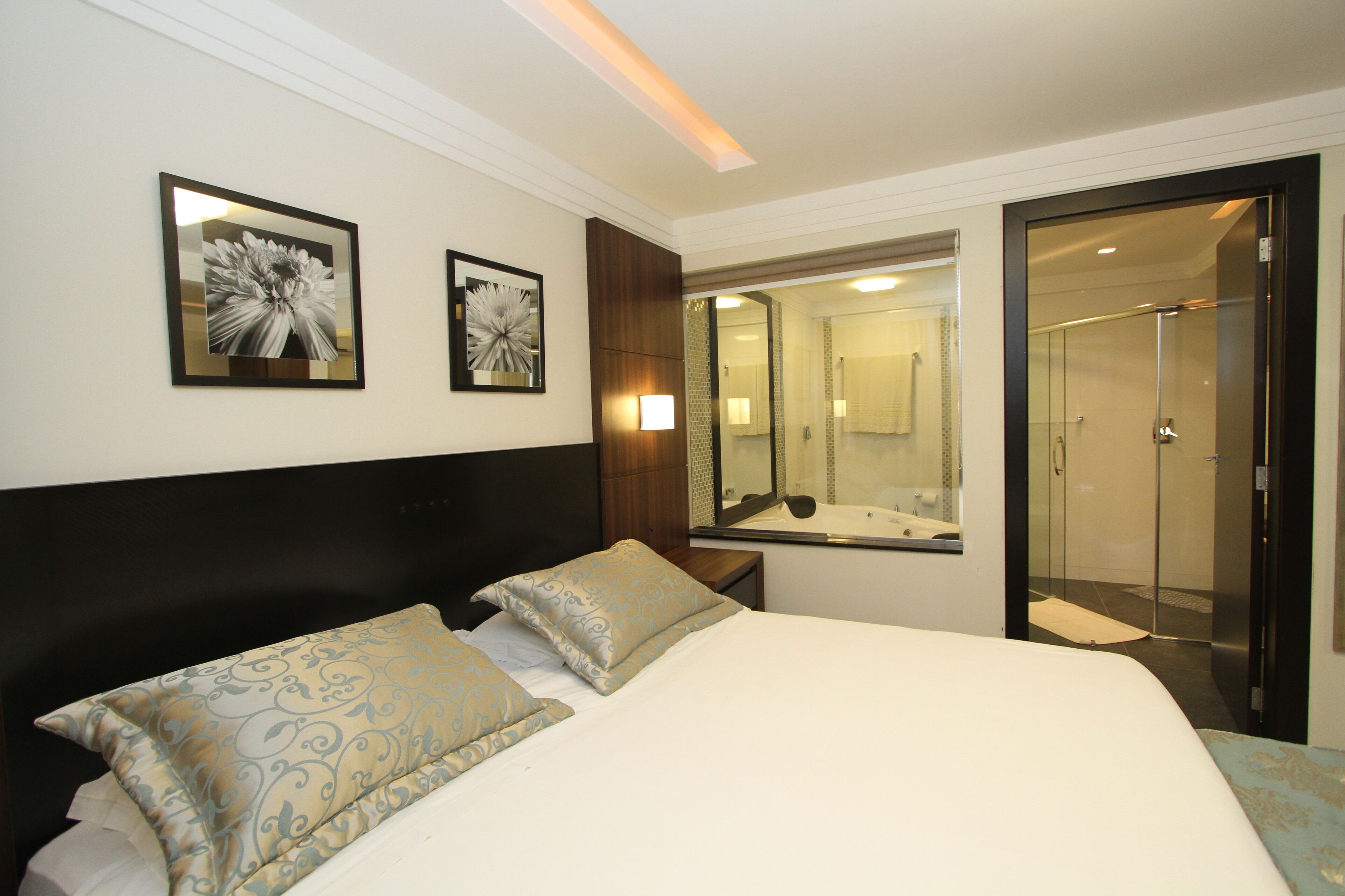 A hotel room with a large bed, two pillows, a nightstand, a mirror, and a walk-in shower.