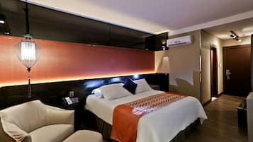 A hotel room with a bed, bedside table, lamp, and a chair.