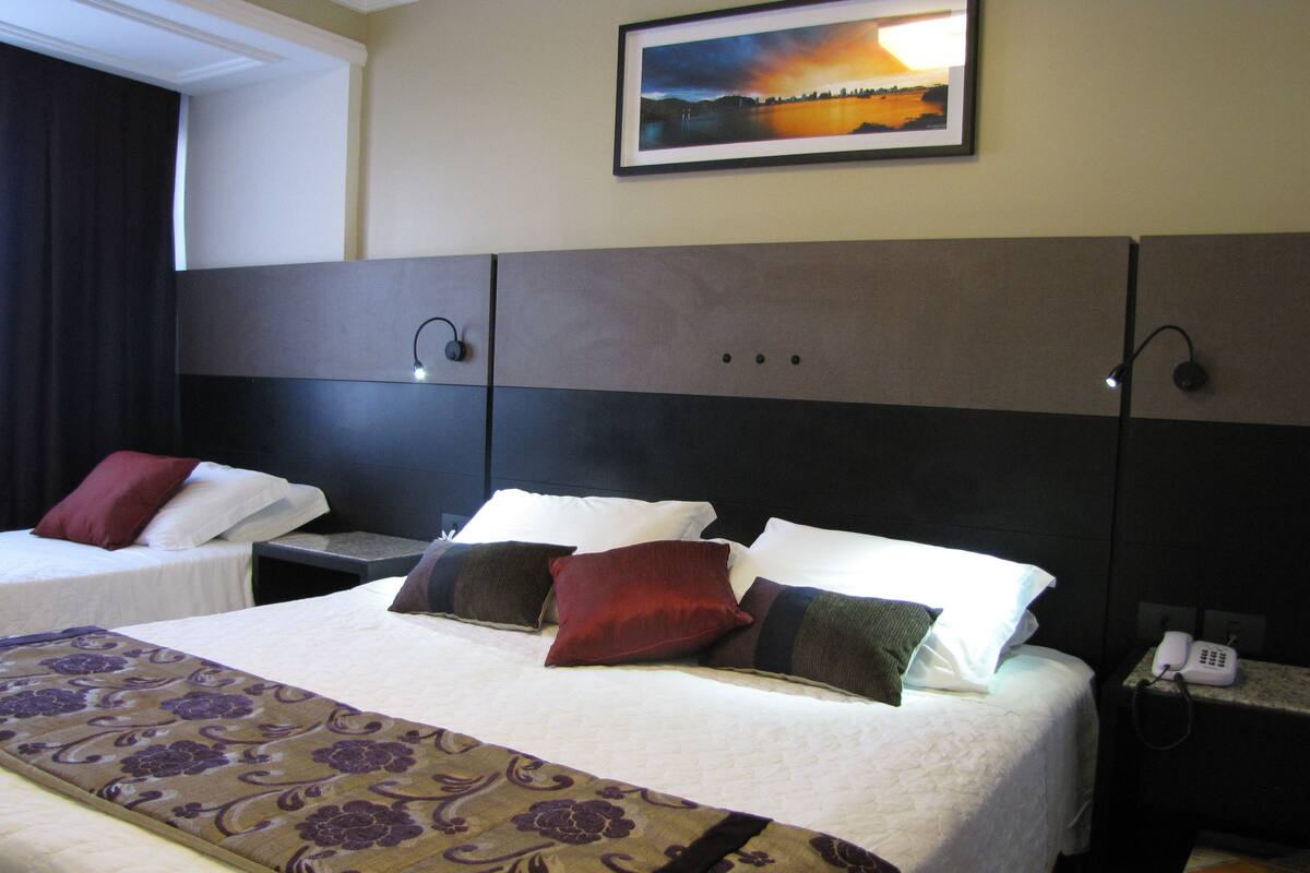 A hotel room with two beds, a large painting on the wall, and a telephone on the nightstand.