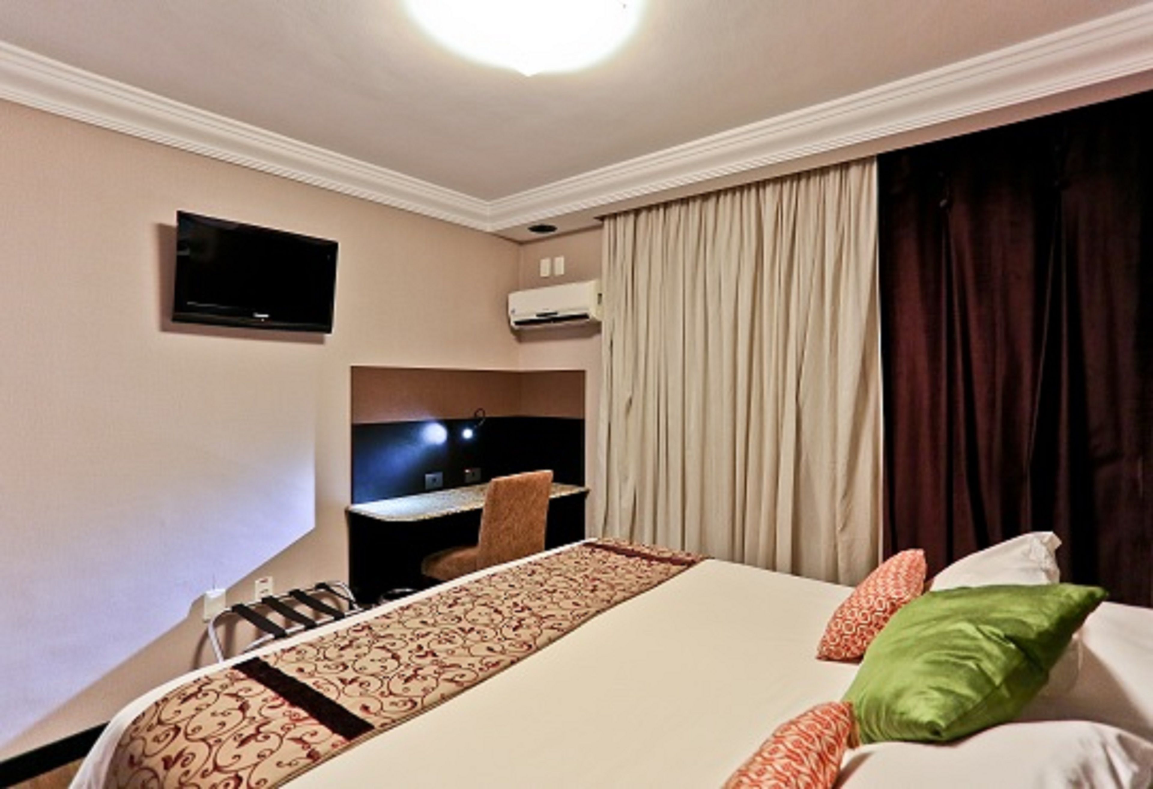 A hotel room with a bed, a desk, a television, and an air conditioning unit.