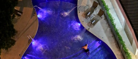 An aerial view of a swimming pool with a unique shape, surrounded by lounge chairs and a small table.