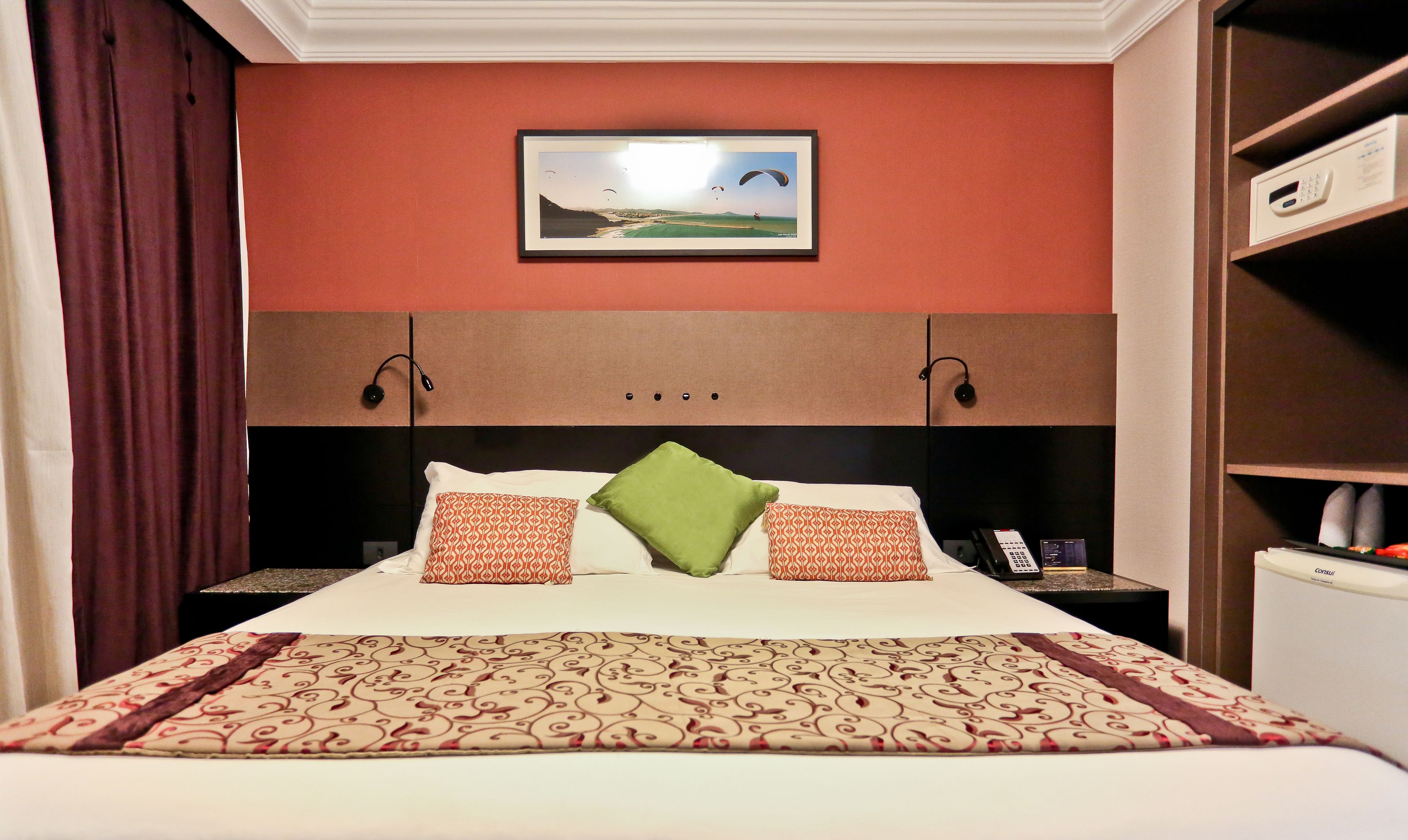 A hotel room with a bed, a TV mounted on the wall, a bedside table with a phone, and a nightstand.