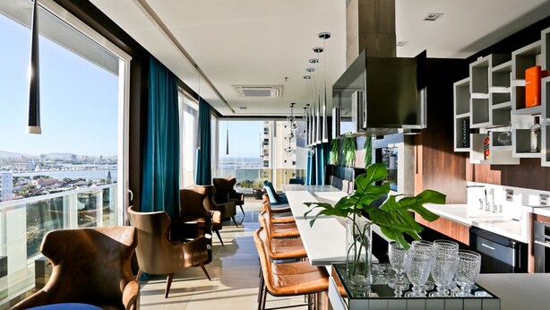 A modern kitchen with a large island, bar seating, and a view of the city. - Sandri Palace Hotel (Itajai)