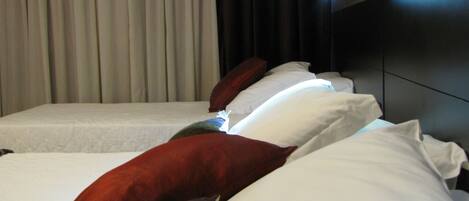Habitación de hotel con dos camas, cada una con sábanas blancas y varias almohadas.