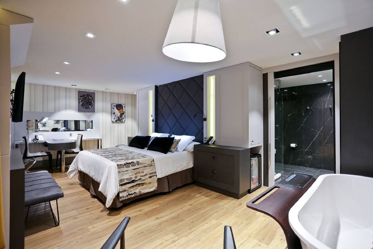 A modern hotel room with a bed, desk, and a glass shower area.