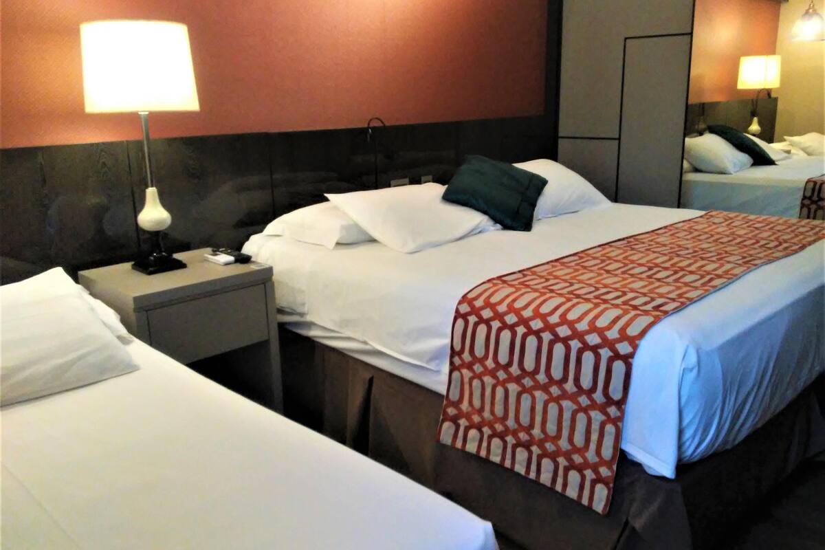 A hotel room with two beds, a nightstand with a lamp, and a mirror.