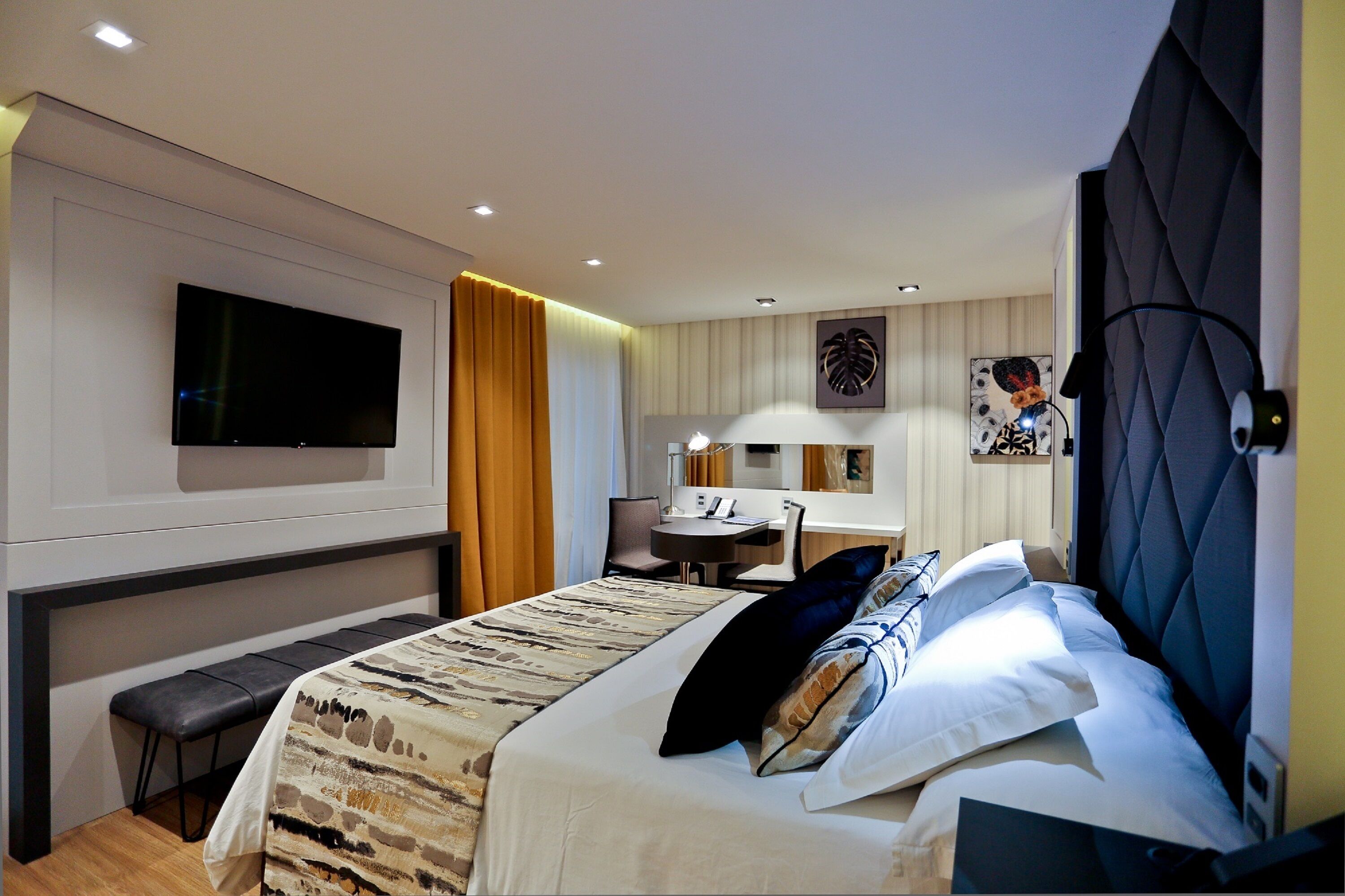 A modern hotel room with a large bed, a desk, a chair, a flat-screen TV, and a large window with curtains.