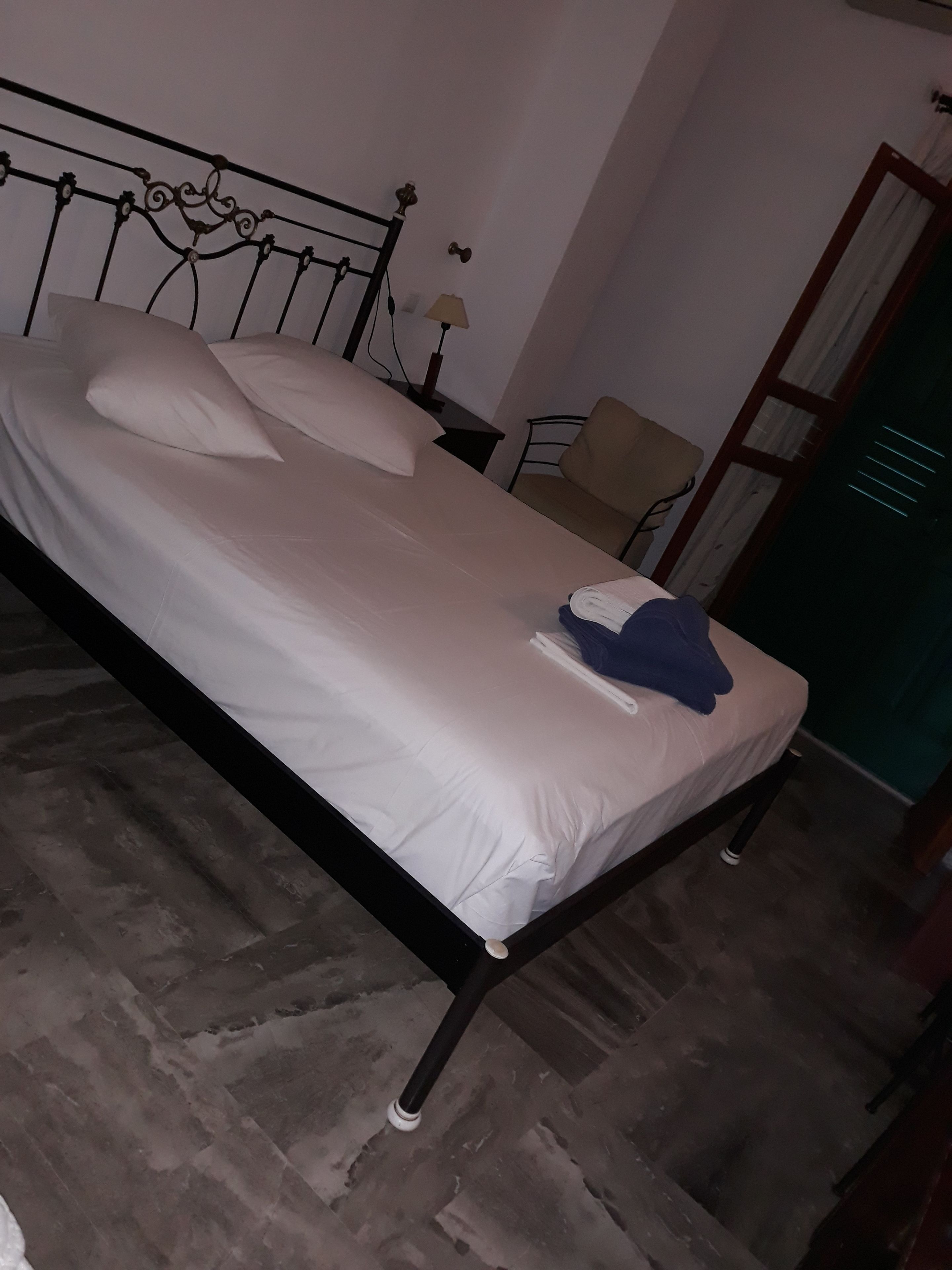 A single bed with a metal frame, white bedding, and a folded towel on the footboard.