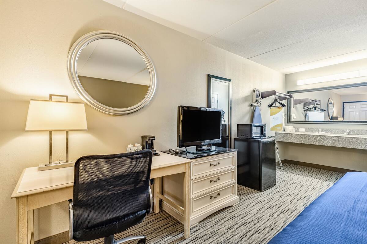 Una habitación de hotel con escritorio, silla, televisión, minibar y cama.