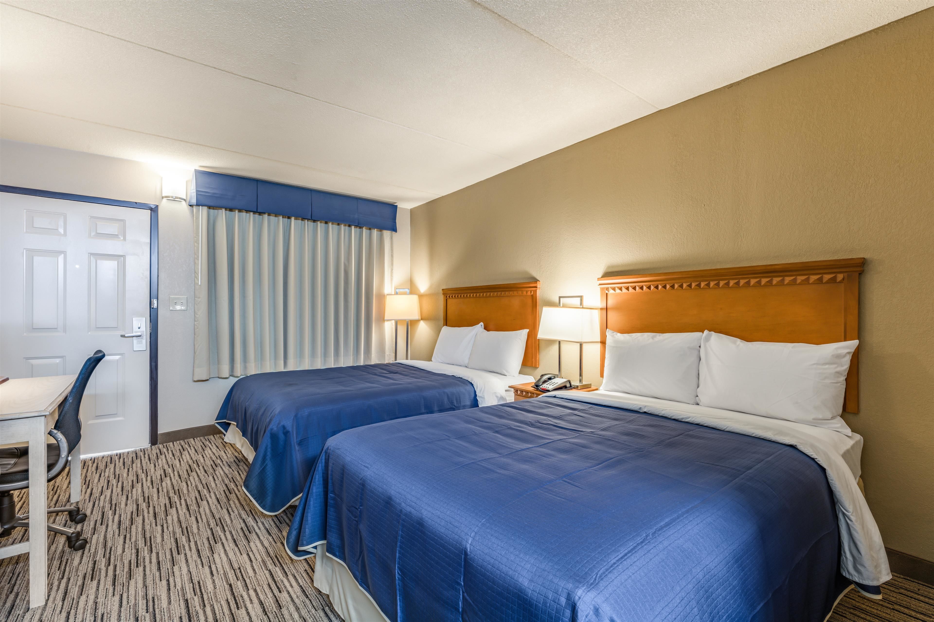 A hotel room with two beds, a desk, and a chair.