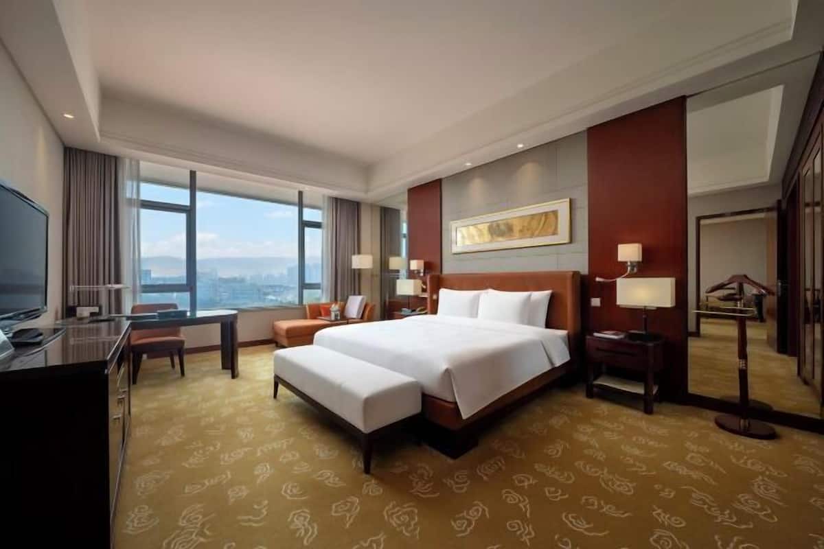 Een hotelkamer met een groot bed, een bureau, een stoel, een televisie en uitzicht op de stad.