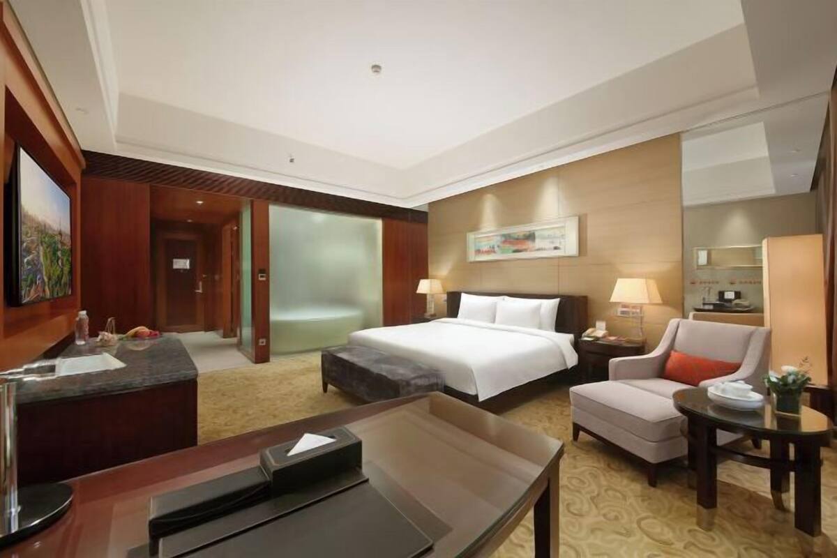 Een hotelkamer met een bed, bureau, stoel, lamp en een schilderij aan de muur.