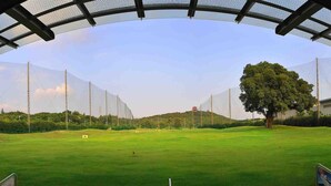 A golf course with a netted viewing area, a flag, and a flagpole. - Quanzhou Guest House Hotel (Quanzhou)