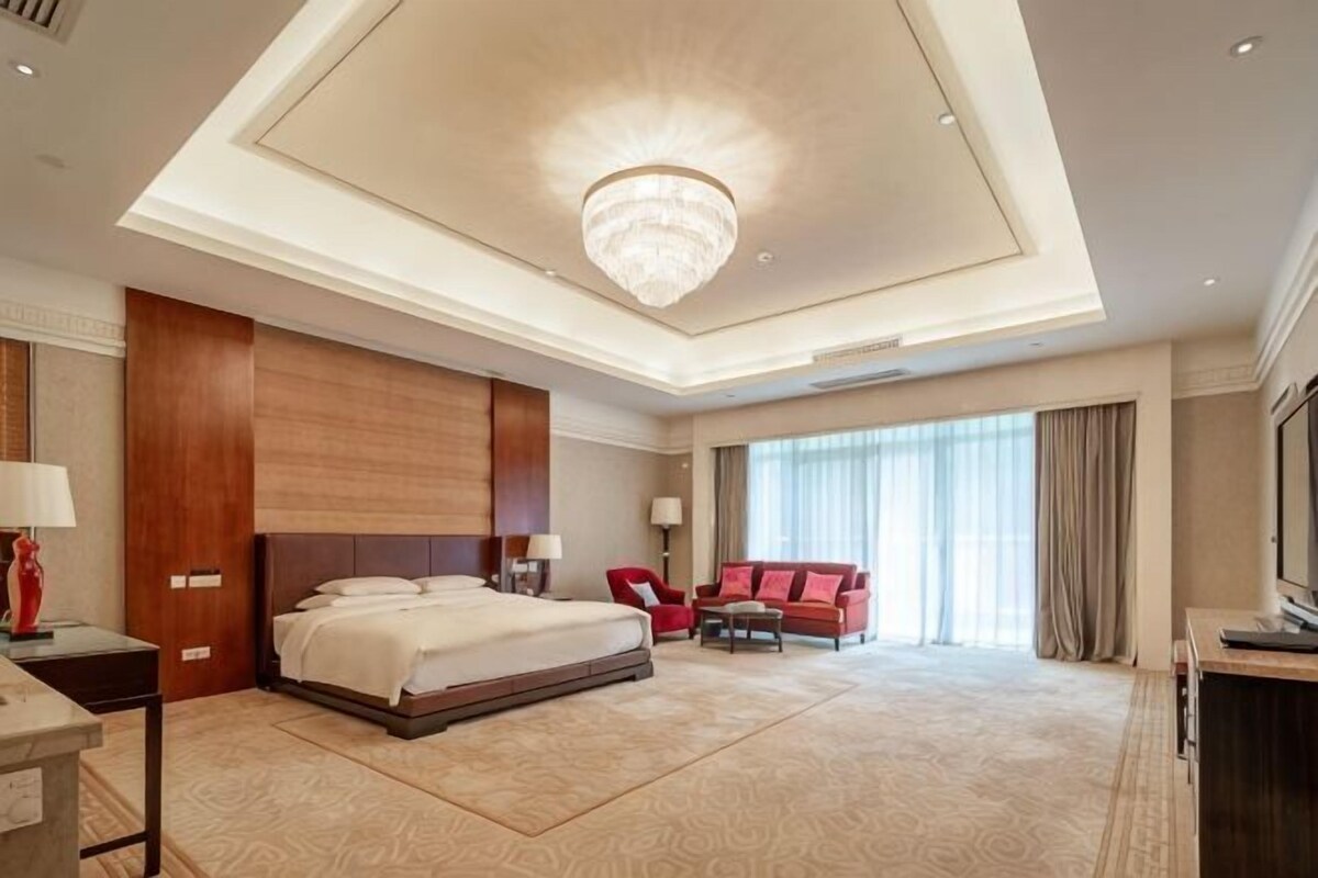 Une chambre d’hôtel spacieuse, dotée d’un grand lit, d’un téléviseur à écran plat, d’un fauteuil rouge et d’un lustre.