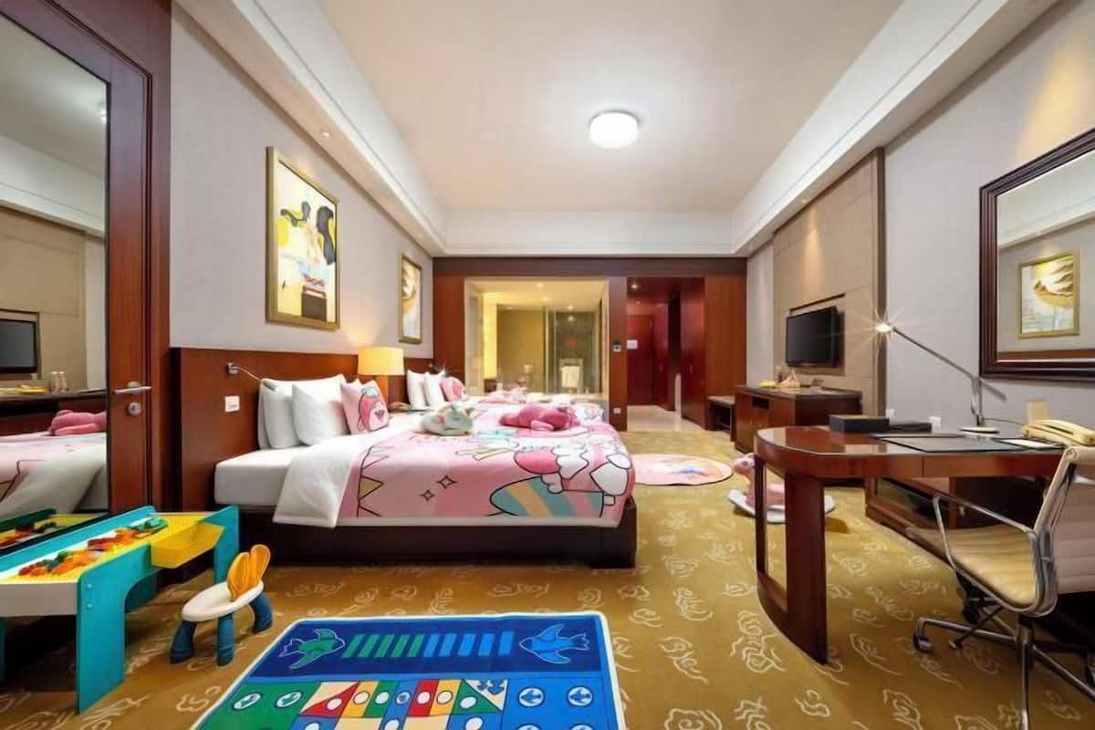 Een hotelkamer met een bed, bureau, stoel en een kinderspeelhoek.