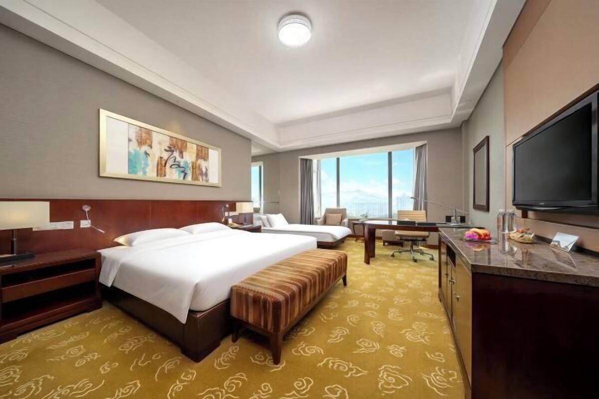 Een hotelkamer met twee bedden, een bureau, een televisie en een groot raam.