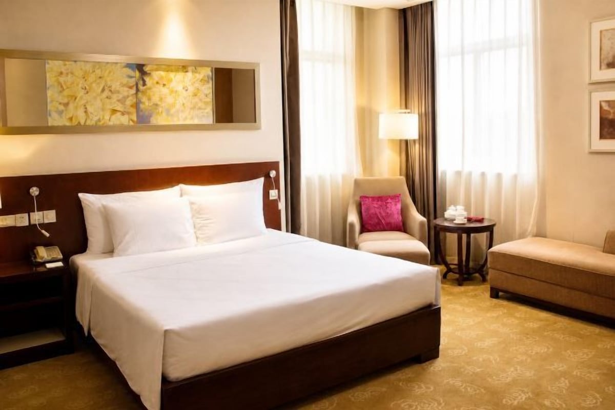 A hotel room with a large bed, a nightstand, a chair, a small table, and a sofa.