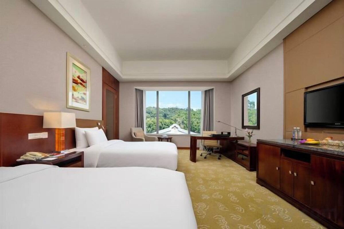 Ein Hotelzimmer mit zwei Betten, einem Schreibtisch, einem Fernseher und Blick ins Freie.