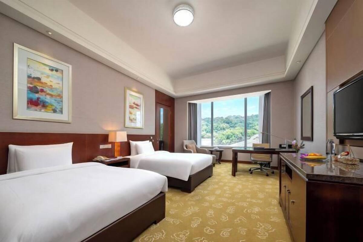 Een hotelkamer met twee bedden, een bureau, een stoel, een televisie en een groot raam met uitzicht.