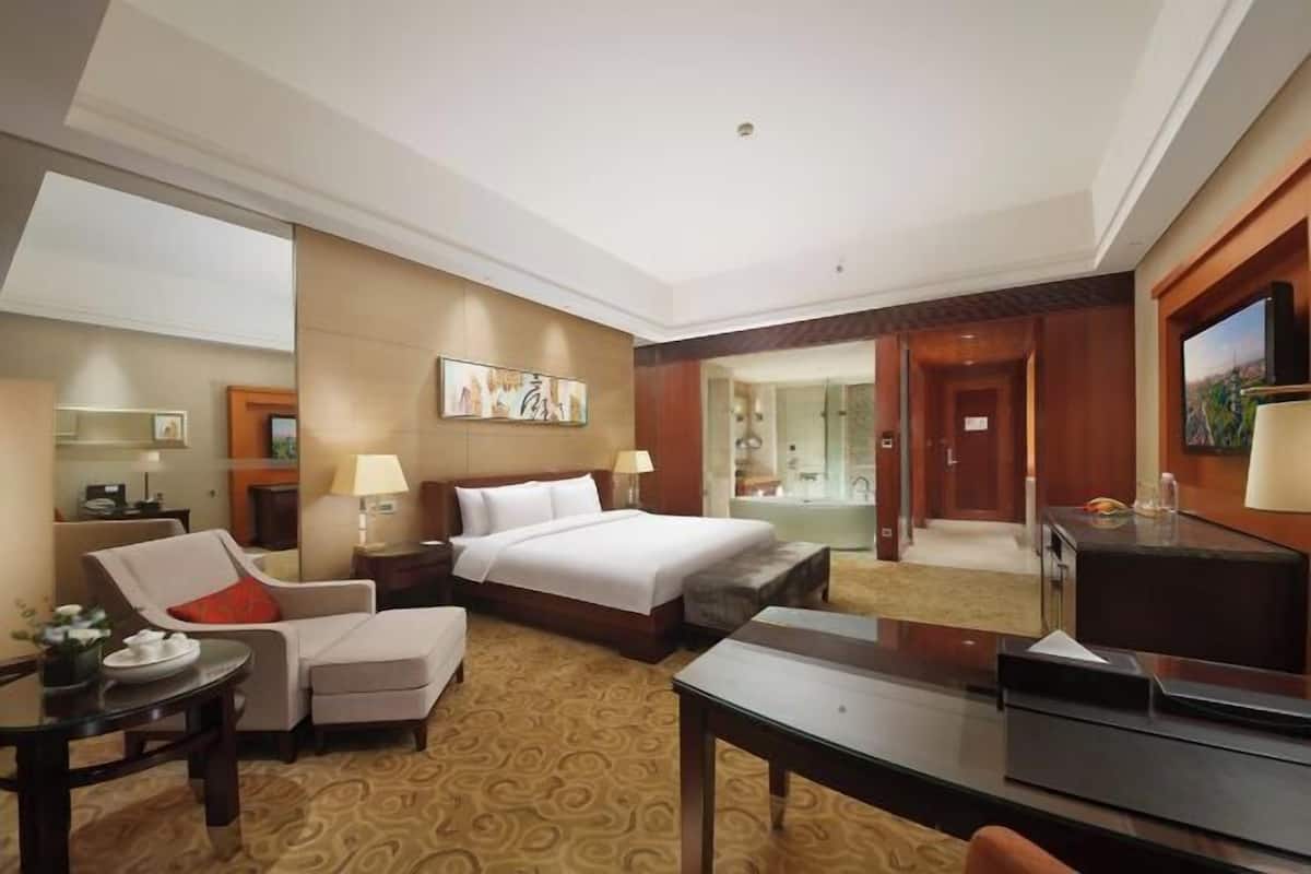 Hotelkamer met een bed, een stoel, een bureau, een televisie en een badkamer die door een open deur zichtbaar is.