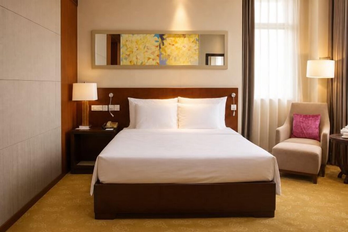 Habitación de hotel con una cama grande, una mesita de noche, una silla y un cuadro en la pared.